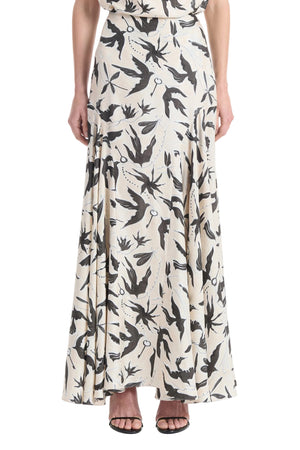 A person wearing the Altuzarra Elton Skirt—a cream, ankle-length skirt with a black bird print and flared silhouette—paired with open-toed black heels.