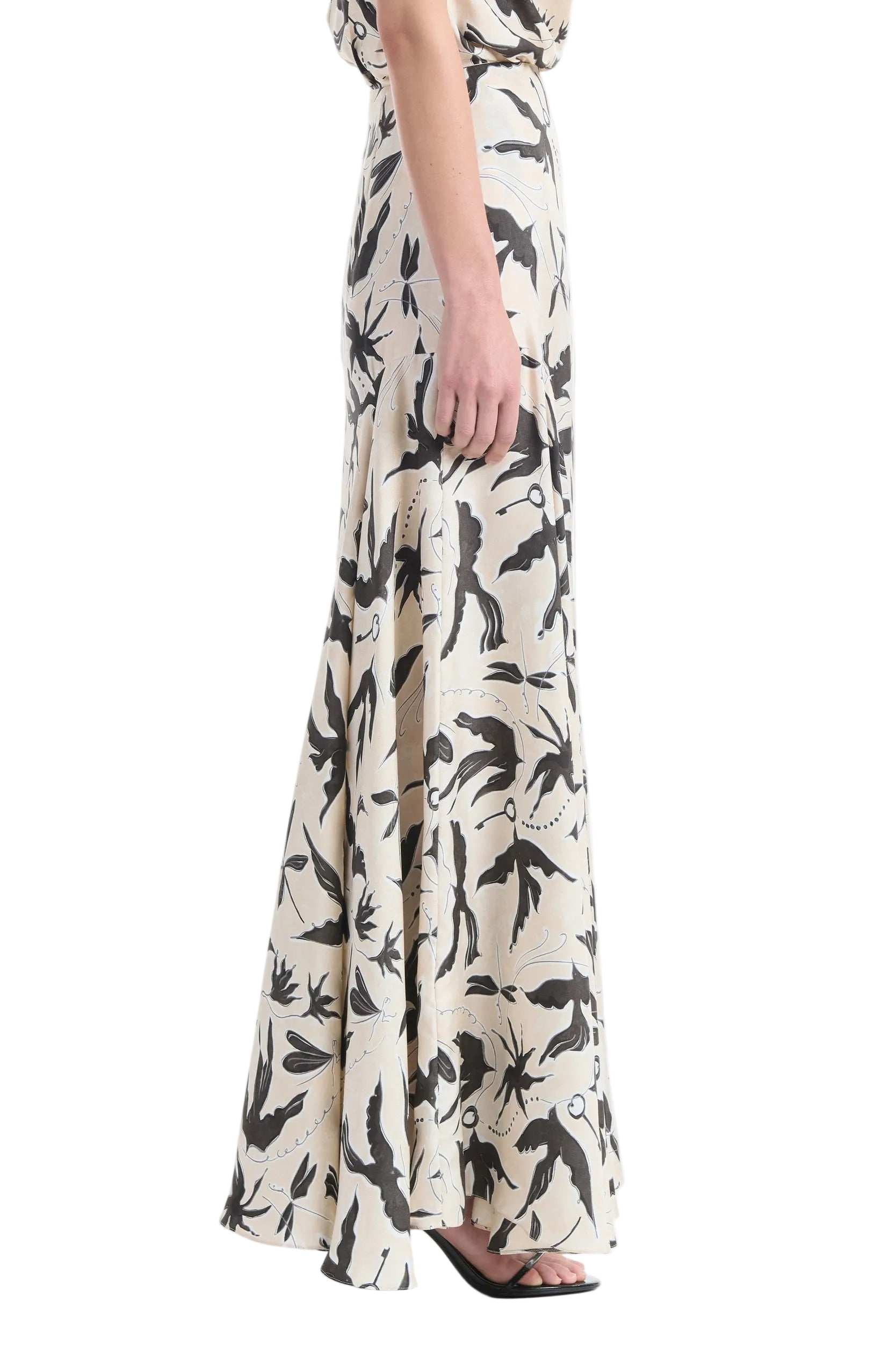 A person stands in profile against a white background, wearing the Altuzarra Elton Skirt—a long, cream skirt with a black abstract print and a fitted waist.