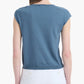 A person is shown from the back wearing the Altuzarra Rinaldi Top—a blue jersey knit short-sleeve shirt—paired with white pants, set against a plain white background.