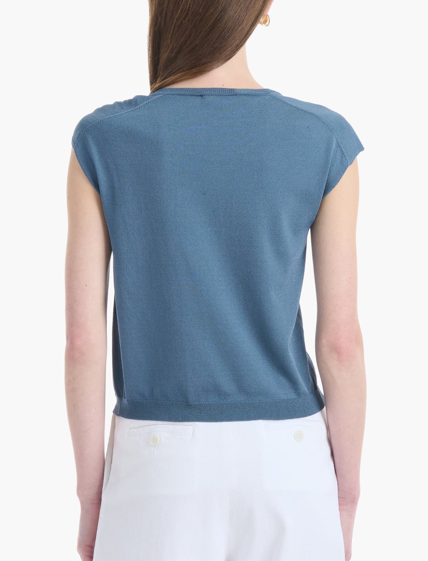 A person is shown from the back wearing the Altuzarra Rinaldi Top—a blue jersey knit short-sleeve shirt—paired with white pants, set against a plain white background.