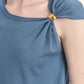A close-up of a person wearing the Altuzarra Rinaldi Top, a blue jersey knit style with gathered shoulders accented by gold metal details.