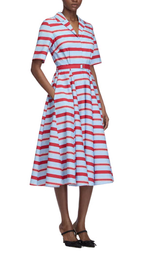 A person is wearing the Emilia Wickstead Mella Bayadere Stripe Dress—a knee-length, short-sleeved summer dress featuring red and white horizontal stripes on a light blue background—paired with black heels.