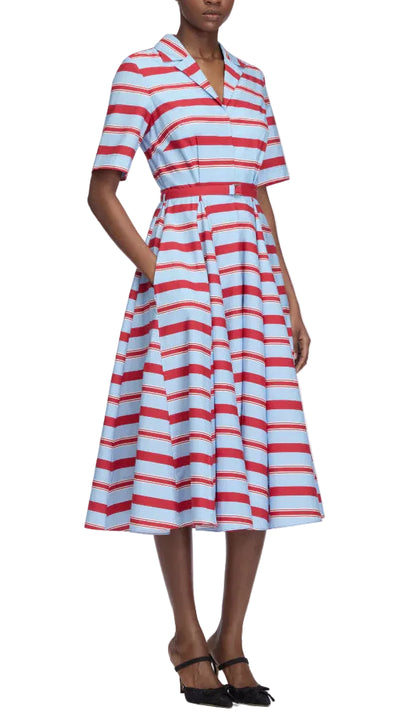 A person is wearing the Emilia Wickstead Mella Bayadere Stripe Dress—a knee-length, short-sleeved summer dress featuring red and white horizontal stripes on a light blue background—paired with black heels.