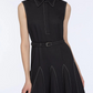 A woman wears the Emilia Wickstead Monique Denim Dress—a sleeveless black collared dress with white stitching, a belted waist, and a flared skirt.