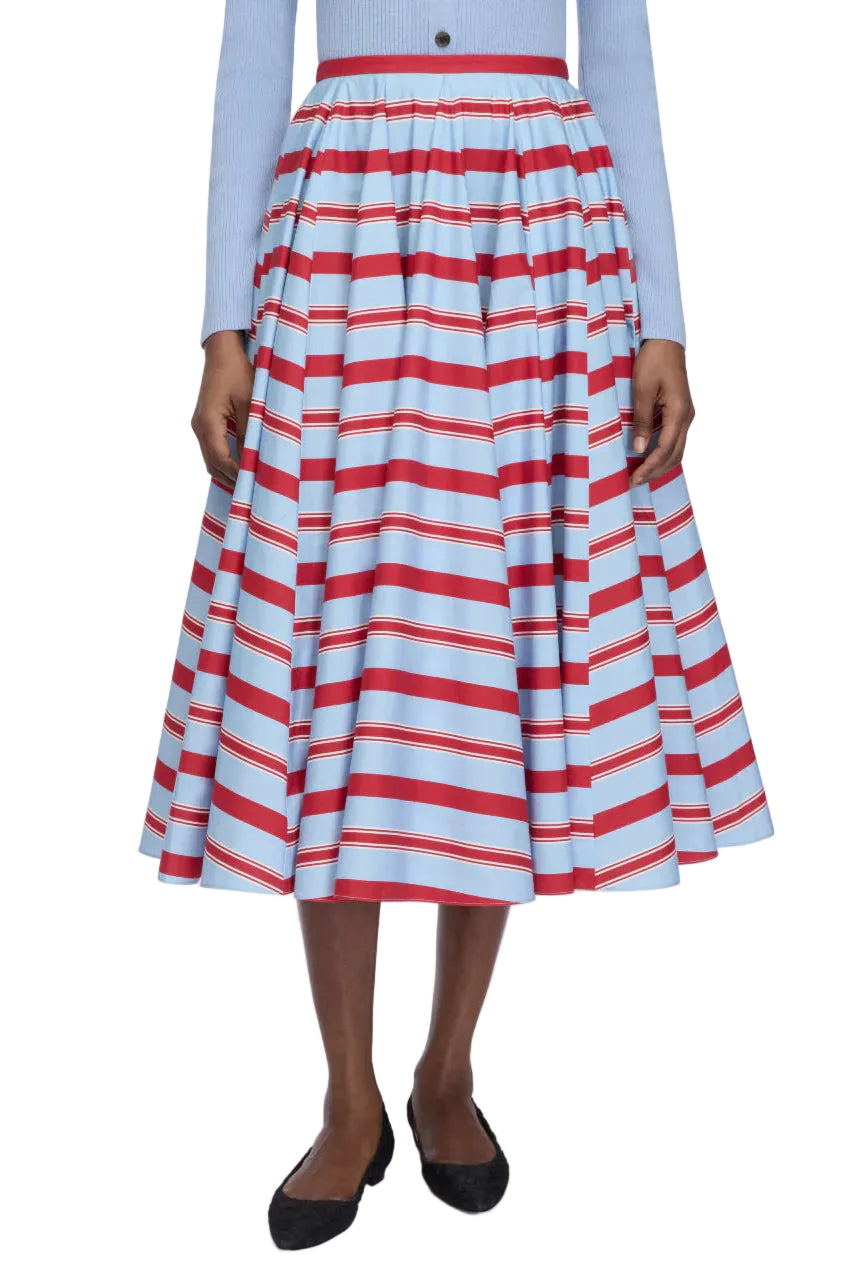 A person wearing a blue long-sleeve top and the Emilia Wickstead Rhea Skirt—a high-waisted, tea-length skirt featuring red and white horizontal stripes—paired with black flats.