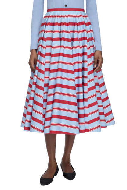 A person wearing a blue long-sleeve top and the Emilia Wickstead Rhea Skirt—a high-waisted, tea-length skirt featuring red and white horizontal stripes—paired with black flats.