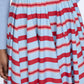 A person wearing a light blue ribbed top tucked into the Rhea Skirt by Emilia Wickstead, a full, pleated cotton skirt featuring horizontal red, white, and blue stripes.