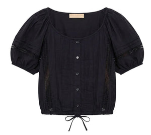 The Clara Top by Ulla Johnson is a black short-sleeve blouse featuring front buttons, pintuck details, delicate Victorian lace accents, a scoop neckline, puffed sleeves, and a drawstring hem.