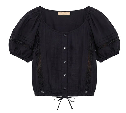 The Clara Top by Ulla Johnson is a black short-sleeve blouse featuring front buttons, pintuck details, delicate Victorian lace accents, a scoop neckline, puffed sleeves, and a drawstring hem.