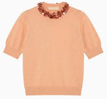 The Jude Embellished Top by Ulla Johnson is a peach merino wool short-sleeve knit sweater with ribbed cuffs and hem, adorned with a decorative beaded necklace detail at the neckline.