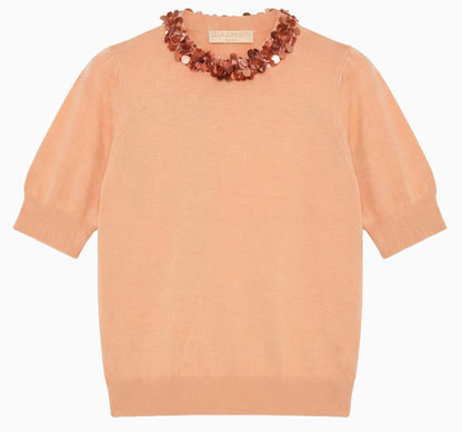 The Jude Embellished Top by Ulla Johnson is a peach merino wool short-sleeve knit sweater with ribbed cuffs and hem, adorned with a decorative beaded necklace detail at the neckline.