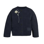 The Flower Jacquard Cropped Jacket by Erdem is a navy blue button-up with two front pockets and white flower embroidery on the left chest, inspired by Erdem’s Pre Fall 2026 collection.