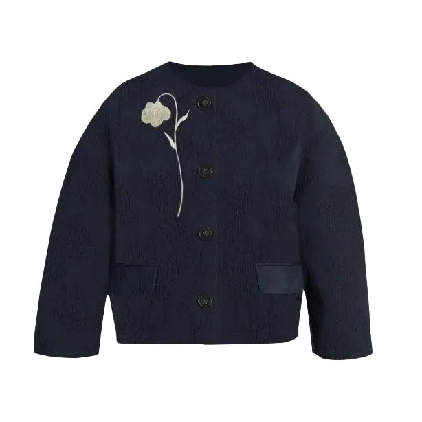 The Flower Jacquard Cropped Jacket by Erdem is a navy blue button-up with two front pockets and white flower embroidery on the left chest, inspired by Erdem’s Pre Fall 2026 collection.