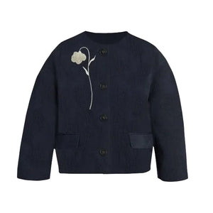 The Flower Jacquard Cropped Jacket by Erdem is a navy blue button-up with two front pockets and white flower embroidery on the left chest, inspired by Erdem’s Pre Fall 2026 collection.