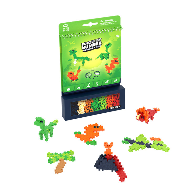 The Plus Plus Puzzle By Number® Activity Pad features a green box, colorful puzzle pieces, and completed pixel-style dinosaurs and a volcano displayed at the front. This engaging kit sparks creativity and helps children develop fine motor skills as they assemble their very own prehistoric scenes.