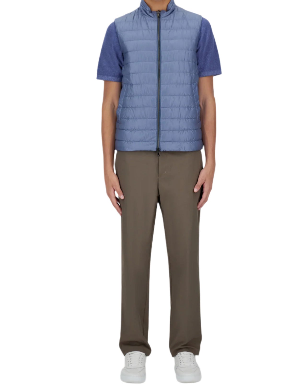 A person stands on a plain background wearing a blue short-sleeve shirt, olive pants, and white sneakers. They sport a stylish Herno Nylon Ultralight Down Reversible Vest, highlighting its water-resistant feature.