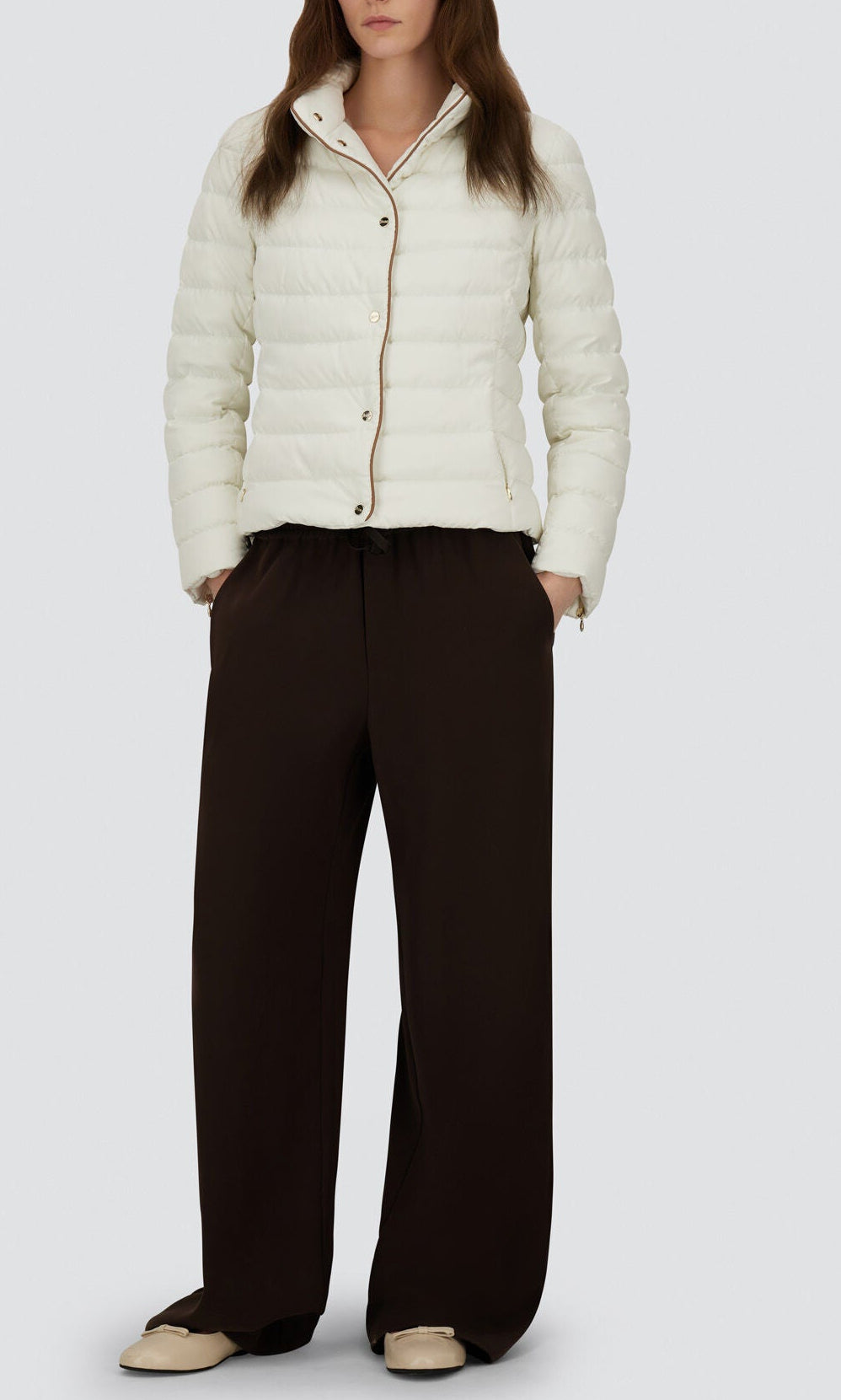 A person wearing the Herno Arendelle Jacket in white, styled with loose dark brown pants and beige shoes, stands against a plain light background.