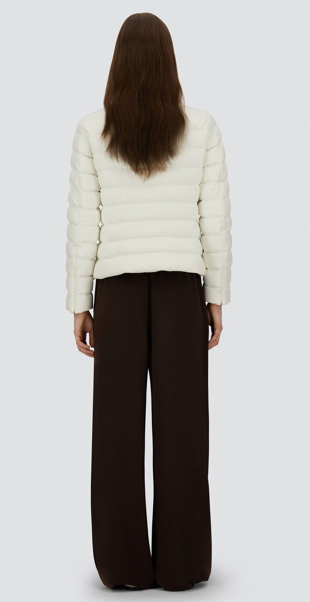 A person stands with their back to the camera, wearing the Herno Arendelle Jacket and wide-leg dark brown pants, set against a plain light gray background.