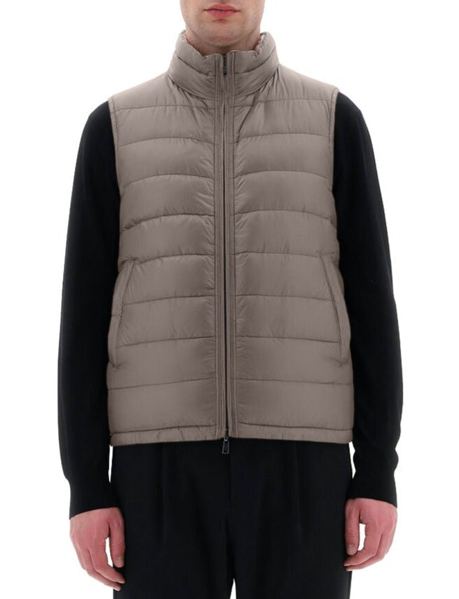 A person is wearing a Herno Men's Nylon Ultralight Reversible Vest, which is light gray, zip-up, and padded with goose down feathers, over a black long-sleeve shirt and black pants.