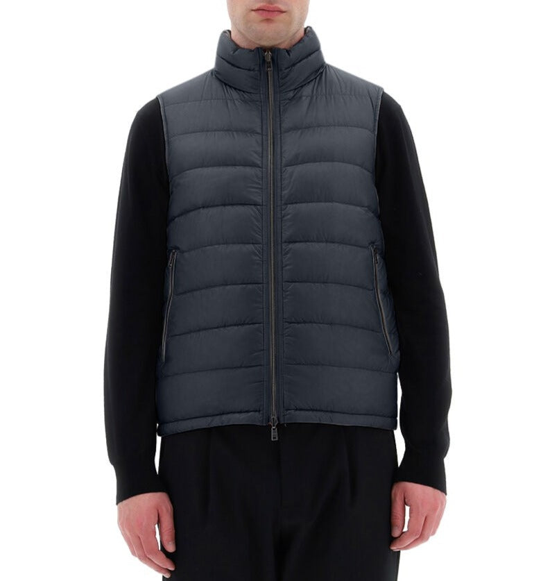 A person wearing the Herno Men's Nylon Ultralight Reversible Vest in dark blue over a black long-sleeve shirt stands against a plain white background.