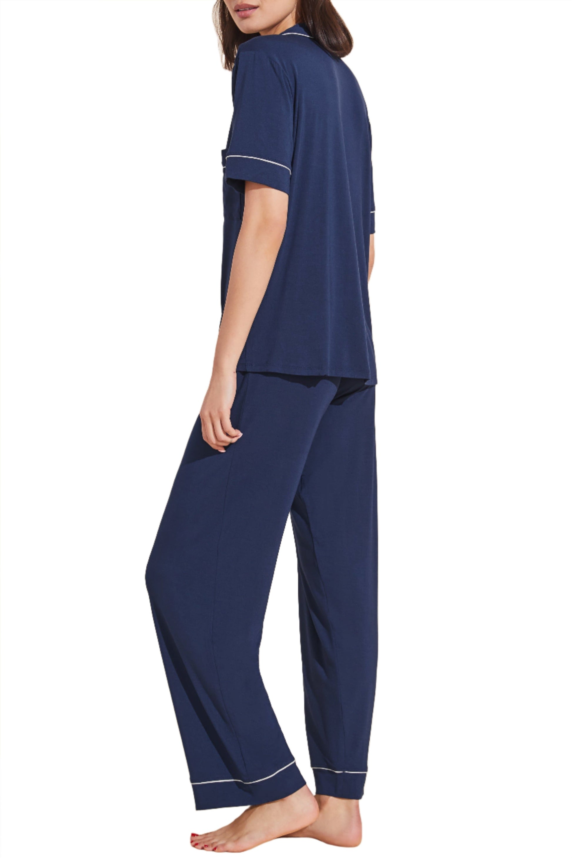 A person wearing a dark blue Eberjey Gisele Short Sleeve Long Pant PJ Set with piping details, crafted from sustainable TENCEL™ Modal, is standing with their back and side to the camera.