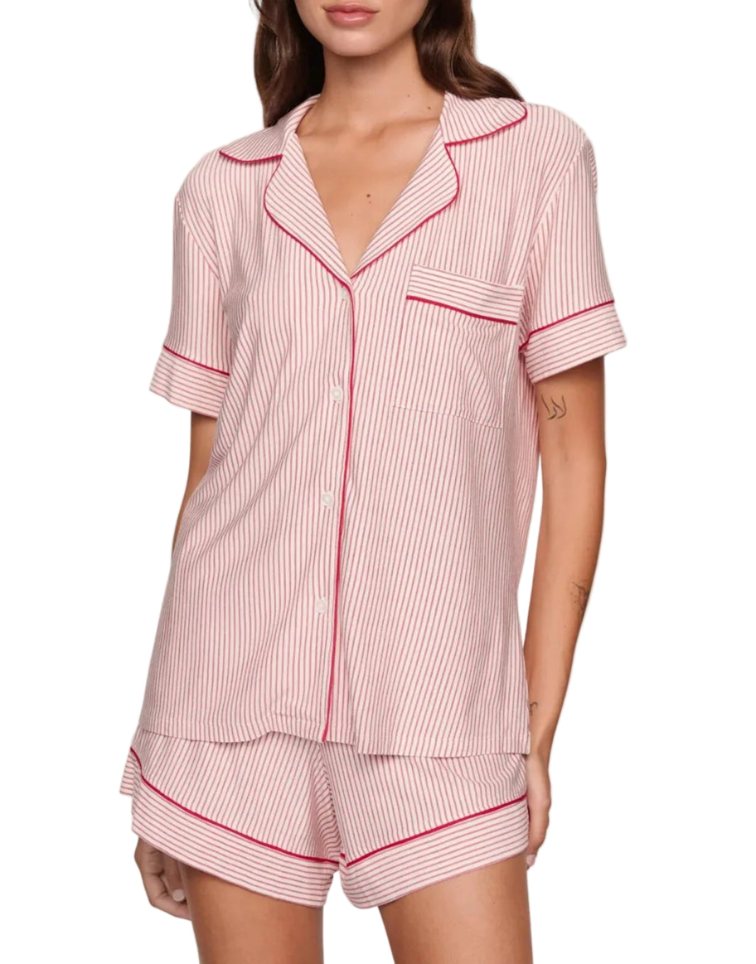A woman wears the Eberjey Gisele Printed Stripe Relaxed Short PJ Set, a buttery soft, cozy sleepwear featuring red and white vertical stripes, red trim, short sleeves, button-up top, and matching shorts.