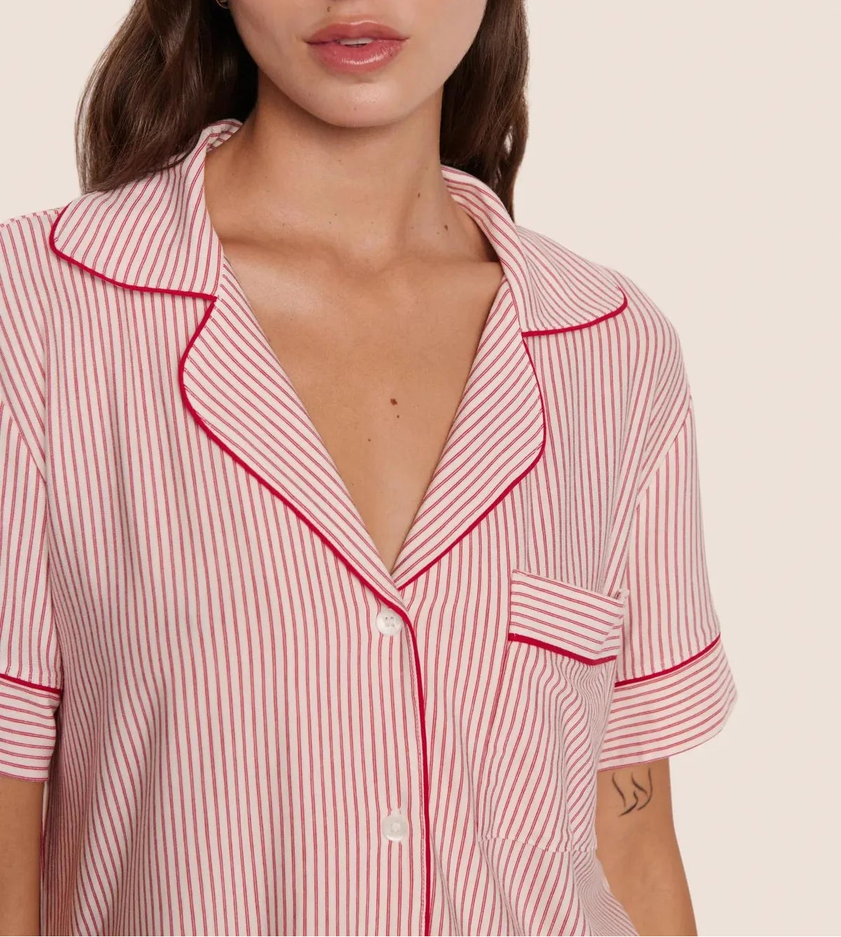 A person wears the Eberjey Gisele Printed Stripe Relaxed Short PJ Set—a pink and white pinstriped pajama top with red piping, buttons, and chest pocket—crafted for ultimate comfort.
