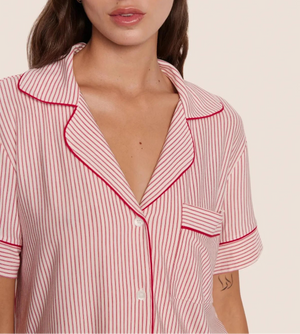 A person wears the Eberjey Gisele Printed Stripe Relaxed Short PJ Set—a pink and white pinstriped pajama top with red piping, buttons, and chest pocket—crafted for ultimate comfort.