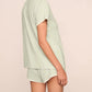 Model in the Eberjey Frida Shortie PJ Set—featuring a slim fit, light green short sleeve top and matching low-rise cheeky shorts with an elastic waistband—posed against a neutral background, shown from the side and back.
