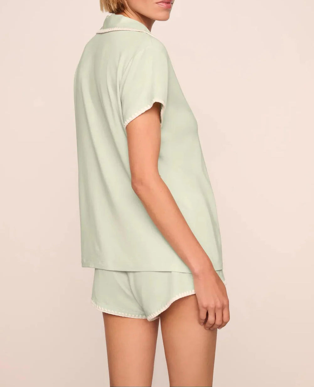 Model in the Eberjey Frida Shortie PJ Set—featuring a slim fit, light green short sleeve top and matching low-rise cheeky shorts with an elastic waistband—posed against a neutral background, shown from the side and back.
