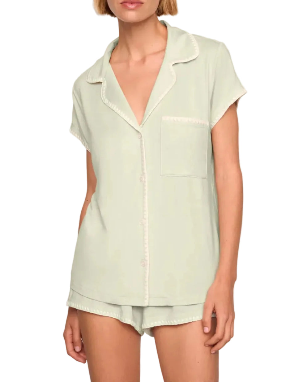 A person wearing the Eberjey Frida Shortie PJ Set: a light green slim fit short sleeve button-up top with a chest pocket, paired with matching low-rise cheeky shorts featuring an elastic waistband.