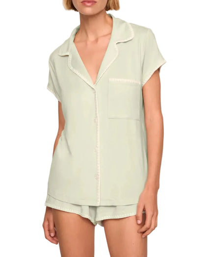 A person wearing the Eberjey Frida Shortie PJ Set: a light green slim fit short sleeve button-up top with a chest pocket, paired with matching low-rise cheeky shorts featuring an elastic waistband.