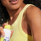 Wearing a yellow tank top, a person sprays Supergoop Play Antioxidant Mist SPF 30 with Vitamin C (6 fl oz) onto their shoulder, revealing glowing skin.