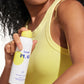 A person in a yellow tank top sprays Supergoop Play Antioxidant Mist SPF 50 with Vitamin C, 6 fl oz, onto their upper arm for glowing skin.