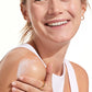 A woman in a white tank top smiles while applying Supergoop Play Everyday Lotion SPF 50 with Sunflower Extract (2.4 oz) to her shoulder.