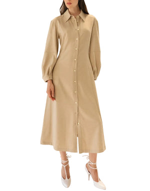 A woman models the Callas Milano Poet Dress—a long beige fit and flare style featuring lantern sleeves—paired with white high-heeled shoes, standing against a white background.