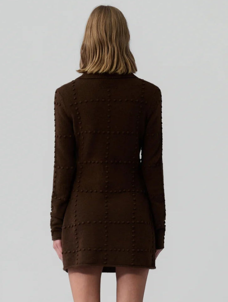 A person with shoulder-length light brown hair is shown from the back wearing Guest in Residence’s Popcorn Polo Dress, a long-sleeve dark brown wool-cashmere blend, against a plain light background.