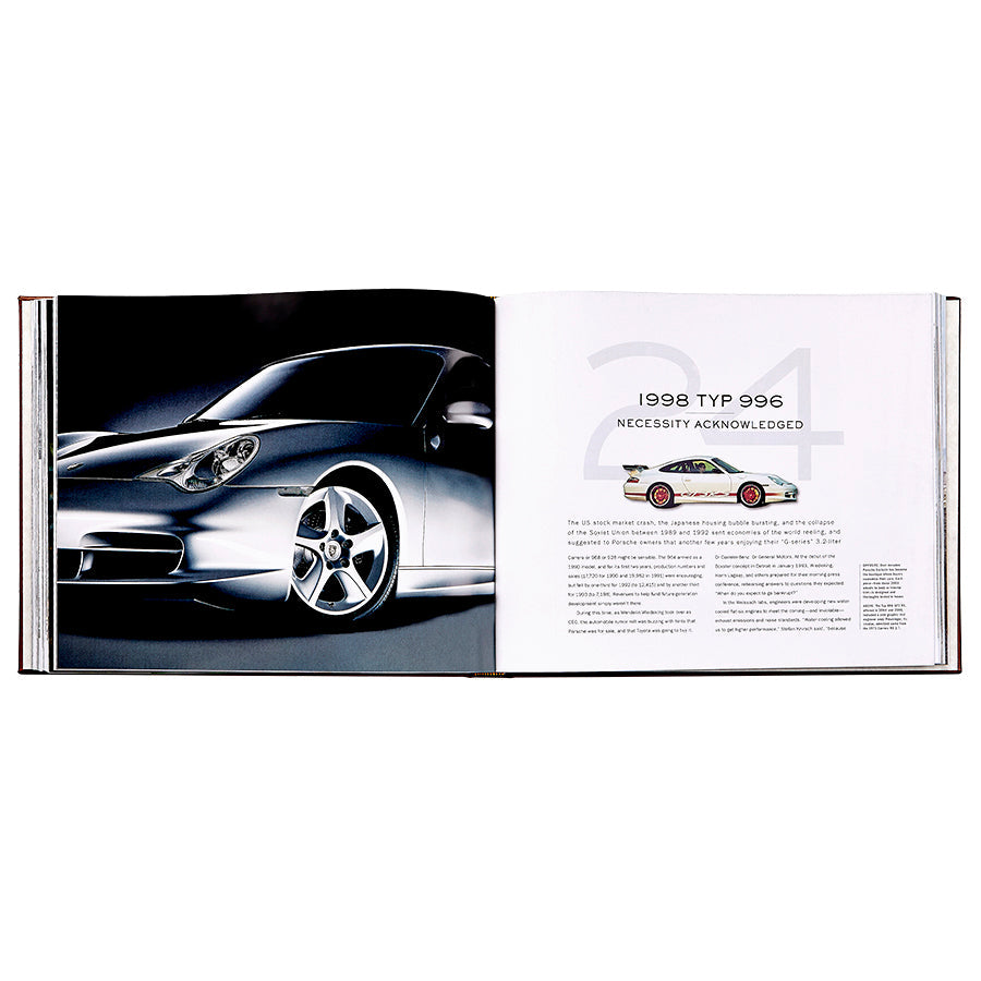 An open book, *Porsche 70 Years: There is No Substitute* by Graphic Image, displays a photo of a silver sports car and text about the 1998 Porsche 996, highlighting a piece of Porsche’s iconic automotive history.