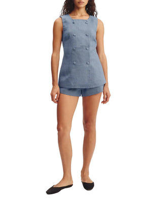 A woman wearing the POSSE Thea Vest, a sleeveless double-breasted linen piece, styled with matching blue shorts and black flats.