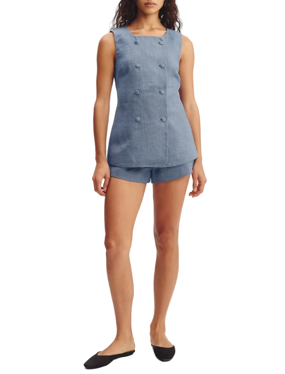 A woman stands with her arms relaxed by her sides, wearing the POSSE Thea Short and a matching sleeveless blue double-breasted top, styled with black flat shoes.