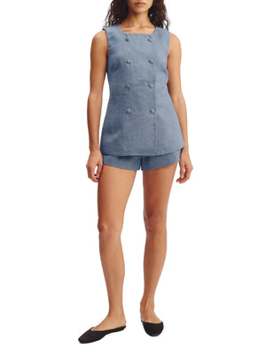 A woman stands with her arms relaxed by her sides, wearing the POSSE Thea Short and a matching sleeveless blue double-breasted top, styled with black flat shoes.