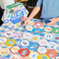 Children practicing their pre-literacy skills work on an alphabet puzzle on a checkered tablecloth, with a box labeled "Eeboo Alphabet Hexagon Pairing Puzzles" nearby.