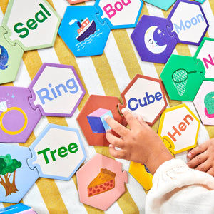 A child arranges Eeboo’s Simple Words Hexagon Puzzle Pairs—colorful pieces with words and matching pictures like "Ring," "Tree," "Cube," and "Moon"—making learning to read a fun, skill-building activity.