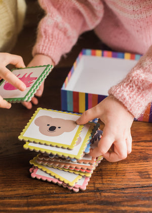 Two children sort animal cards by a colorful box on a wooden table—Eeboo’s Pre-School Animal Memory & Matching Game, designed to build memory and matching skills while engaging young minds.