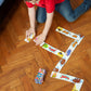 A boy in a red shirt kneels on a wooden floor, arranging Eeboo’s Animal Parade Head to Toe Dominoes in a winding pattern, making this classic game by Eeboo into a fun travel adventure.