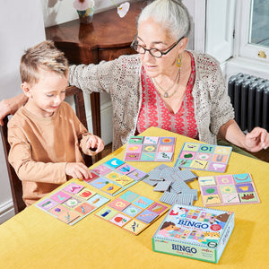 An older woman and a young boy enjoy playing Eeboo's Preschool Things I Know Bingo, a colorful vocabulary-building game with illustrated cards and square tiles that’s perfect for fun family time.