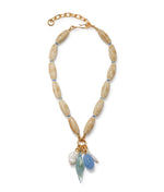 The Marilla Necklace by Lizzie Fortunato features tan oval beads, a gold chain extender, and five assorted blue, white, and gold charms for an ocean-inspired touch.