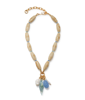 The Marilla Necklace by Lizzie Fortunato features tan oval beads, a gold chain extender, and five assorted blue, white, and gold charms for an ocean-inspired touch.