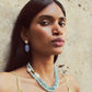 A woman with long dark hair wears a green dress and the Lizzie Fortunato Cabana Necklace, a blue single-strand piece.