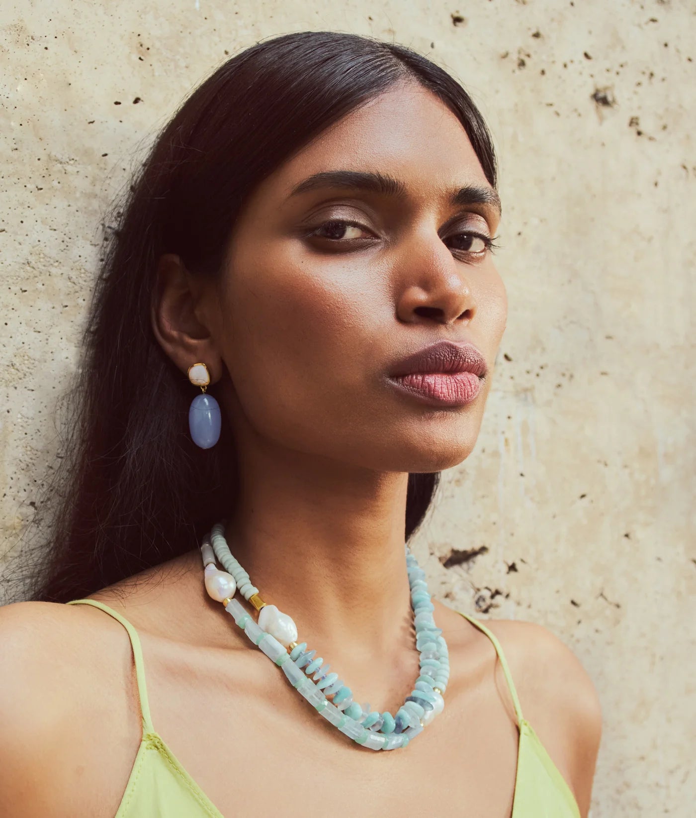 A woman with long dark hair wears a green dress and the Lizzie Fortunato Cabana Necklace, a blue single-strand piece.